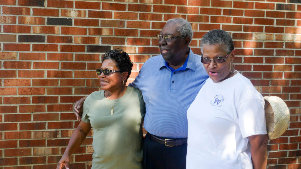 Three people standing in front of a brick wall.